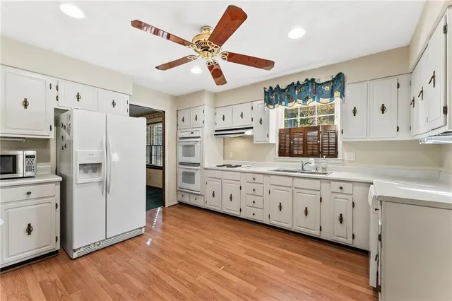 a kitchen with stainless steel appliances granite countertop a refrigerator a sink dishwasher and white cabinets with wooden floor