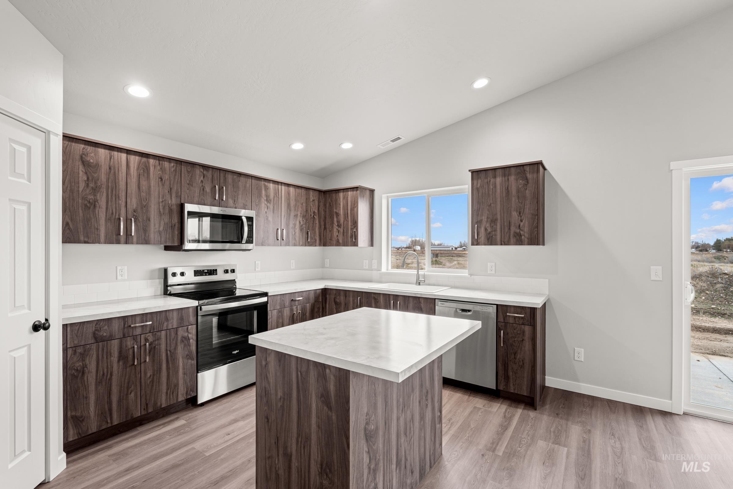 1449 Covington Street Middleton, ID 83644 - Photo 5 of 21 Kitchen featuring light countertops, stainless steel appliances, dark wood finish cabinetry, vaulted ceiling, and light wood-type flooring