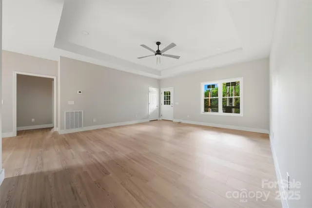 an empty room with wooden floor ceiling fan and windows