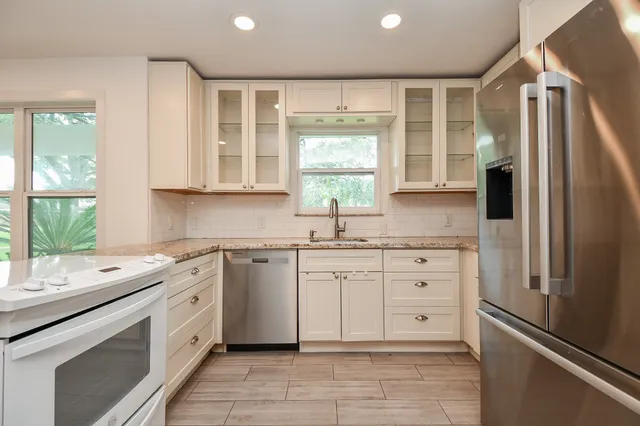 a kitchen with granite countertop white cabinets white stainless steel appliances a sink and a large window
