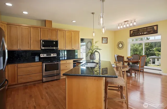 a kitchen with stainless steel appliances granite countertop a stove top oven a sink dishwasher a dining table and chairs with wooden floor