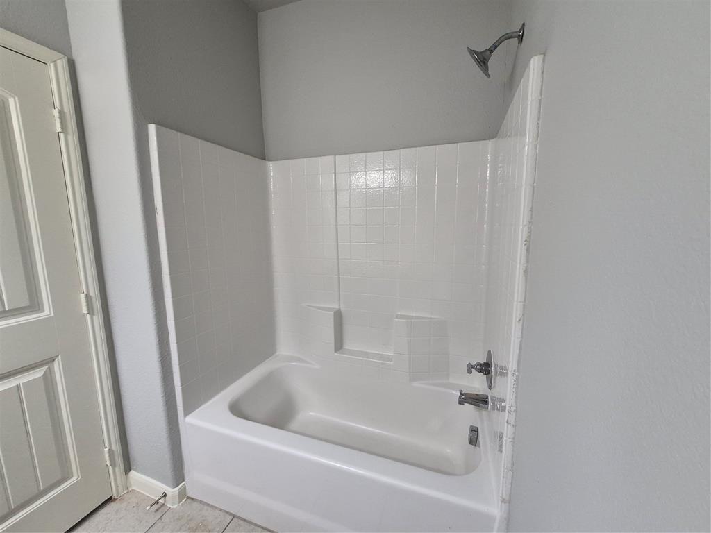 8050 Privet Street Forney, TX 75126 - Photo 19 of 24 The bathroom features a white bathtub with a tiled surround, a chrome showerhead, and a chrome faucet set