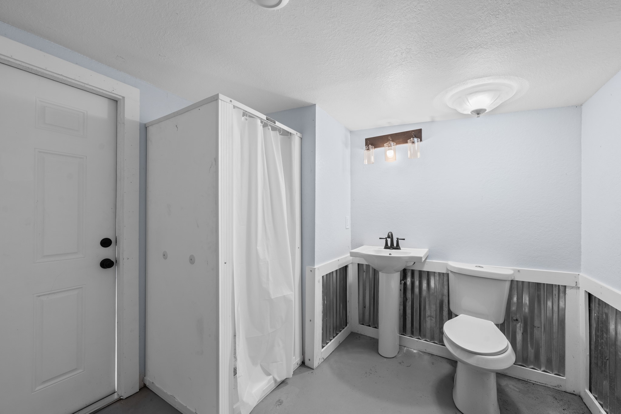 2534 Bastrop Angleton, TX 77515 - Photo 28 of 50 Convenient downstairs bathroom located within the storage area, featuring a walk-in shower, pedestal sink, and durable concrete flooring. Functional layout adds flexibility for outdoor use, workshop access, or additional utility space.