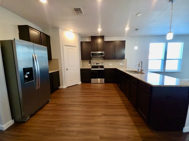 a large kitchen with stainless steel appliances a refrigerator a sink dishwasher a stove and black cabinets next to a window