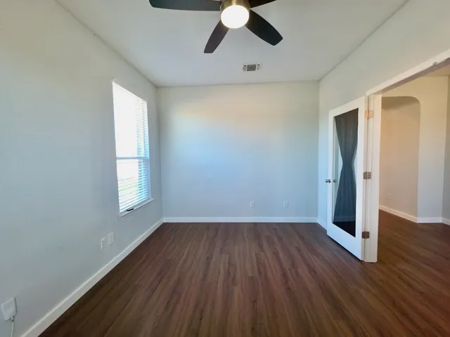 an empty room with wooden floor chandelier fan and windows