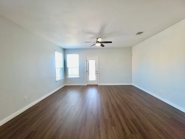 a view of an empty room with wooden floor and window