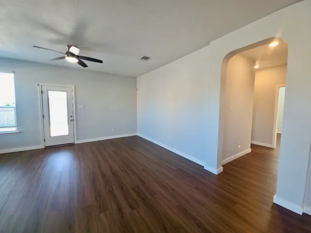 an empty room with wooden floor chandelier fan and windows