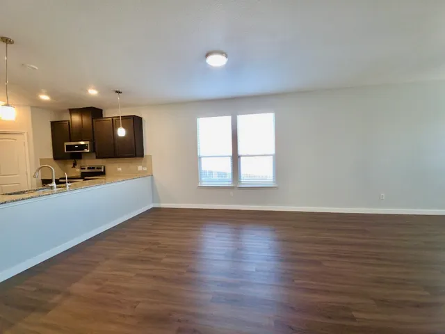 a view of an empty room with kitchen and wooden floor