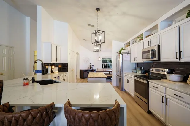 a kitchen with stainless steel appliances kitchen island granite countertop a sink dishwasher and white cabinets with wooden floor