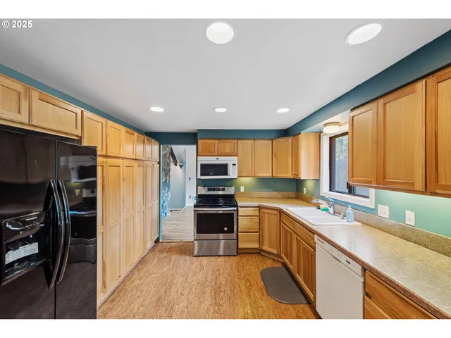 a kitchen with stainless steel appliances granite countertop a refrigerator a sink dishwasher a stove and white countertops with wooden floor