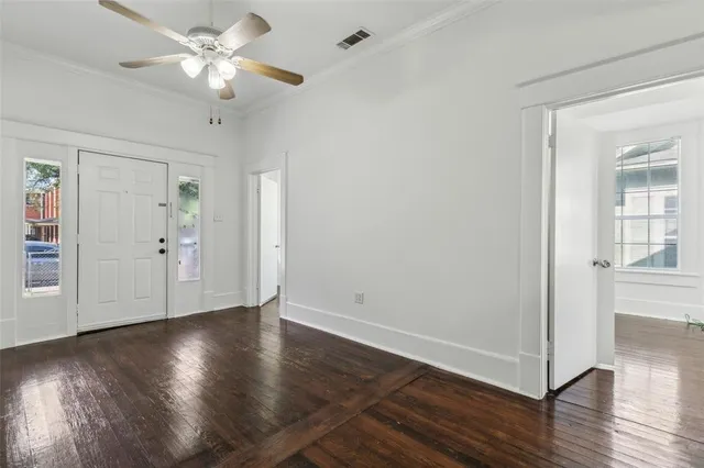 an empty room with wooden floor chandelier fan and windows