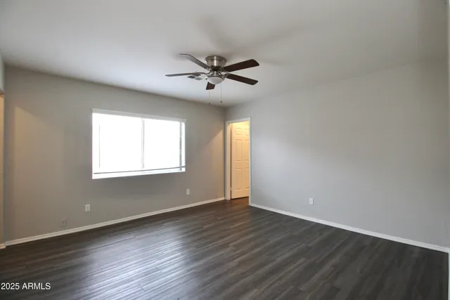 an empty room with wooden floor ceiling fan and windows