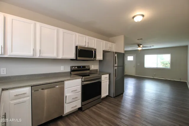 a kitchen with stainless steel appliances granite countertop a stove a sink and white cabinets with wooden floor