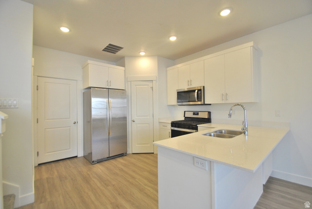 1219 West 1870 South Logan, UT 84321 - Photo 3 of 18 Kitchen featuring stainless steel appliances, a peninsula, light wood-style flooring, white cabinets, and light stone counters