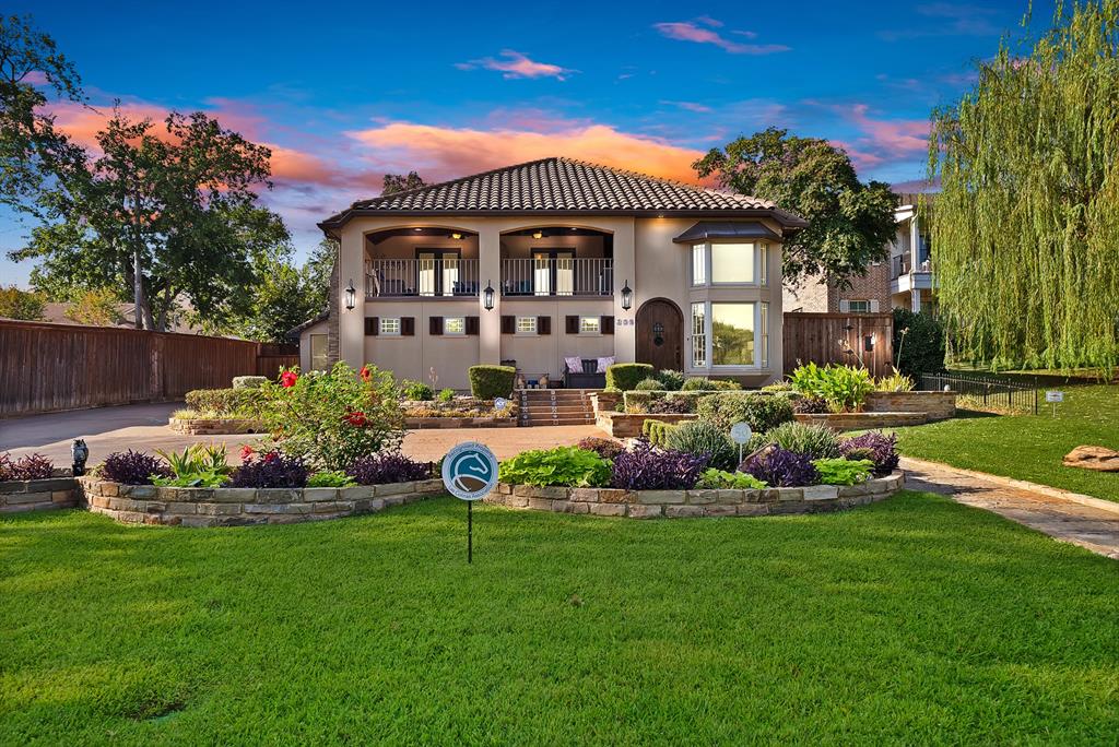 306 Rochelle Boulevard Irving, TX 75062 - Photo 1 of 40 Stucco exterior with a tile roof, featuring a circular driveway, tiered landscaping with stone retaining walls, and a large front lawn