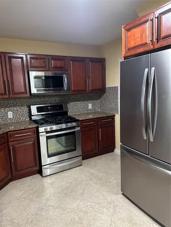 a kitchen with granite countertop a stove top oven a sink dishwasher and a refrigerator with wooden cabinets