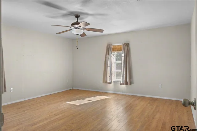 an empty room with wooden floor fan and windows