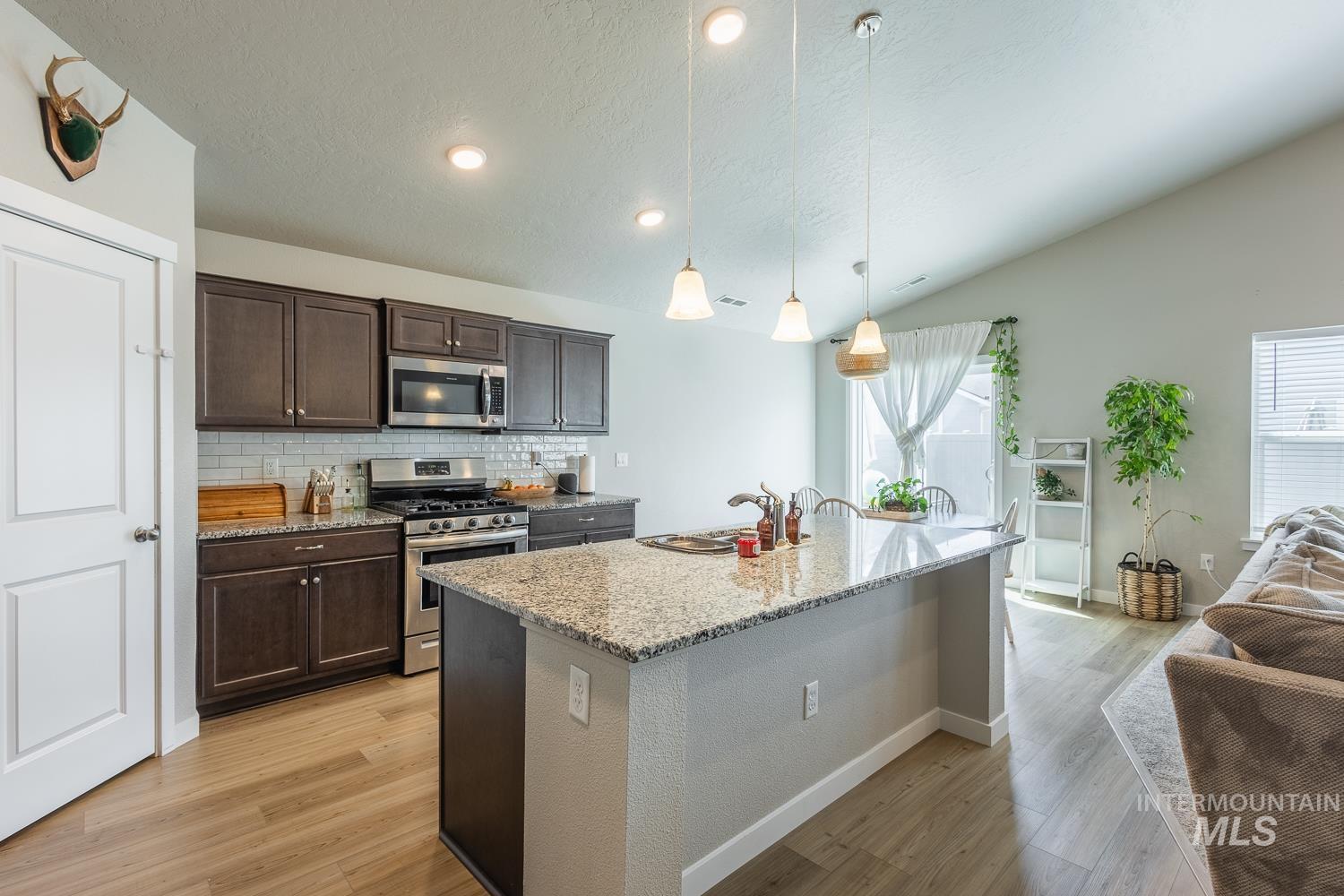 12623 Shadow Peak Street Caldwell, ID 83607 - Photo 13 of 50 Modern kitchen featuring dark wood cabinetry, stainless steel appliances, granite countertops, and a subway tile backsplash