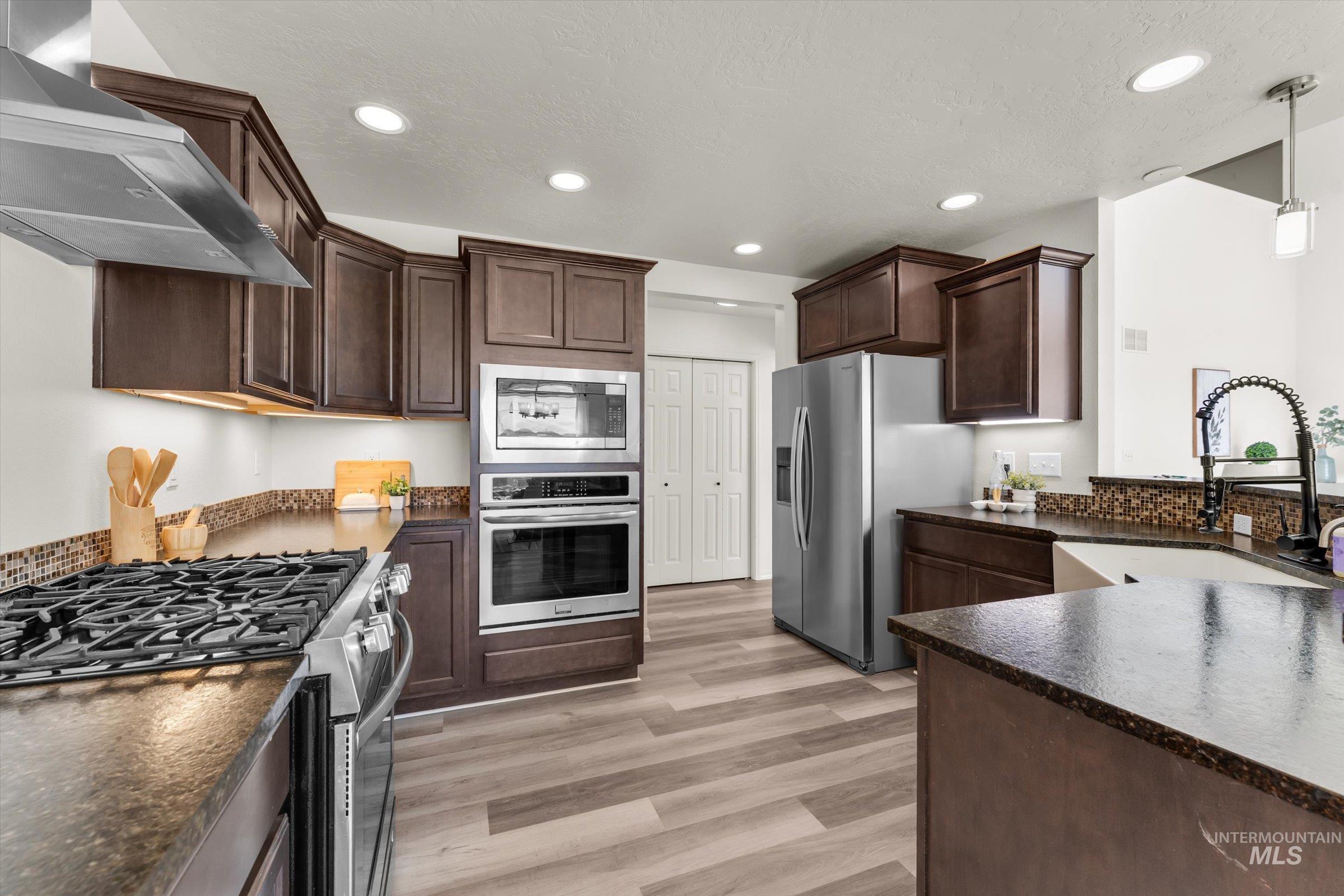 5602 Barkley Way Caldwell, ID 83607 - Photo 12 of 36 Kitchen with stainless steel appliances, dark wood finish cabinetry, pendant lighting, and light wood-type flooring