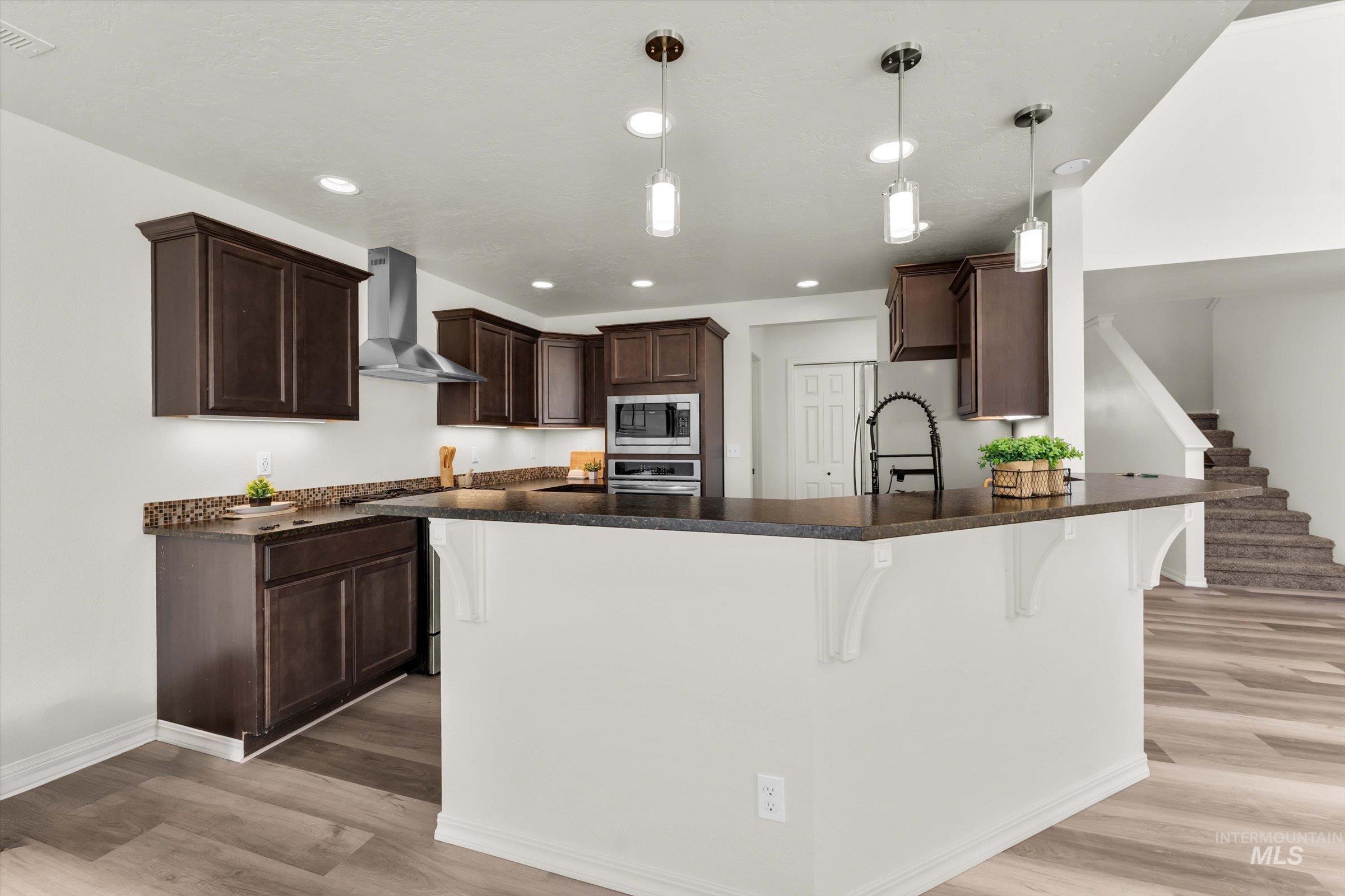 5602 Barkley Way Caldwell, ID 83607 - Photo 8 of 36 Kitchen with a kitchen bar, dark wood finish cabinetry, hanging light fixtures, and light wood-type flooring