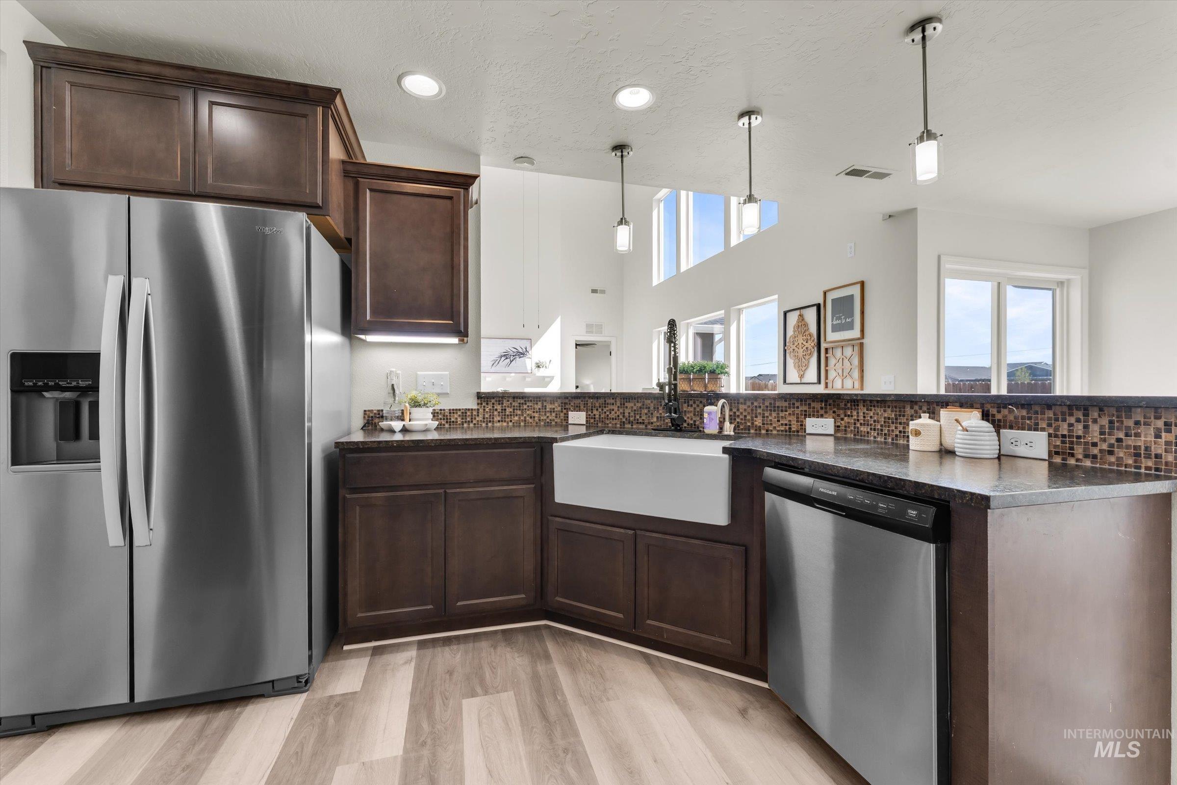 5602 Barkley Way Caldwell, ID 83607 - Photo 9 of 36 Kitchen featuring dark wood finish cabinets, stainless steel appliances, light wood-style flooring, pendant lighting, and a peninsula
