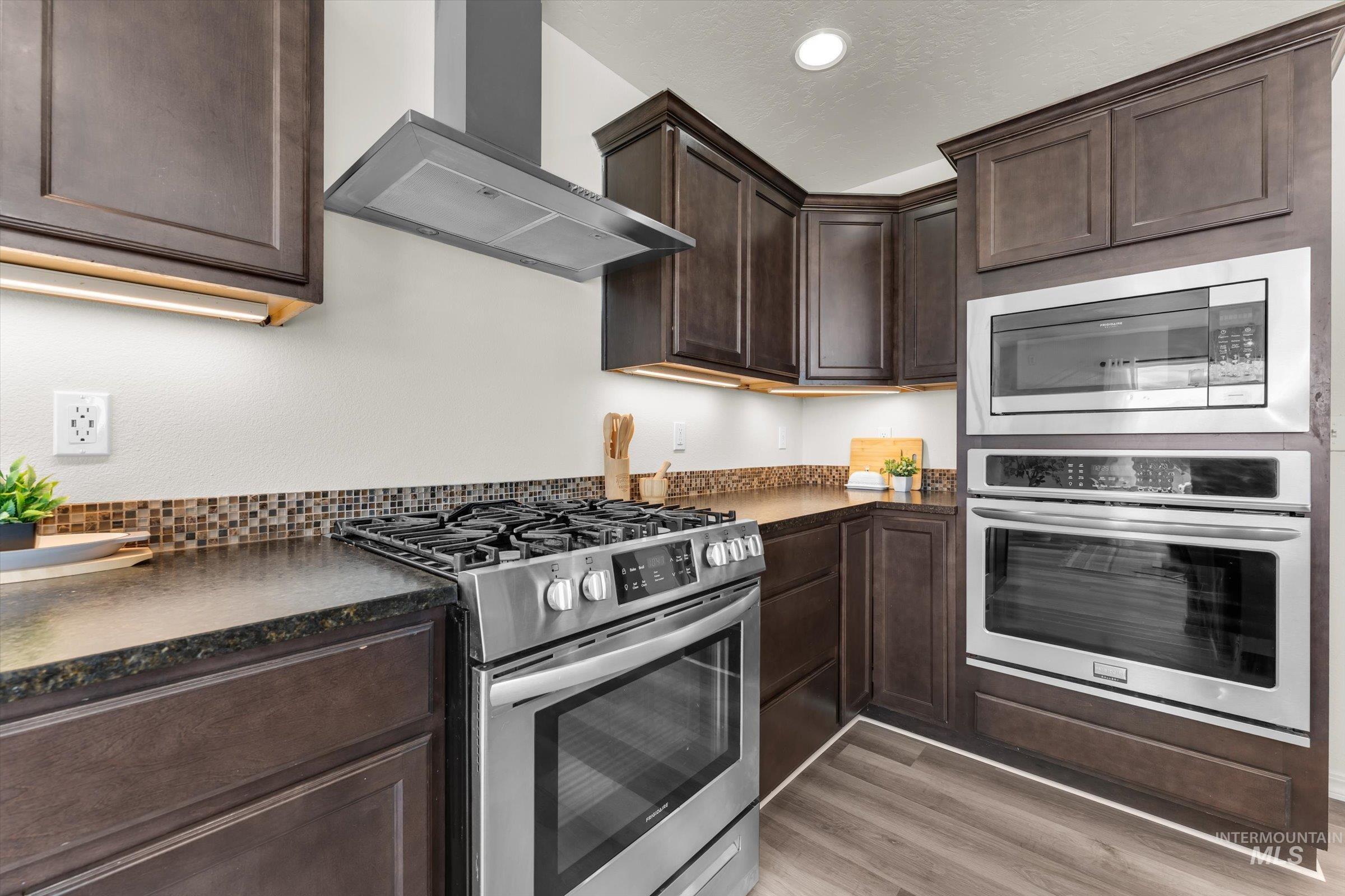 5602 Barkley Way Caldwell, ID 83607 - Photo 10 of 36 Kitchen with stainless steel appliances, dark wood finish cabinetry, dark stone countertops, light wood-style flooring, and recessed lighting