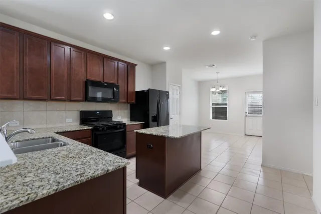 a kitchen with kitchen island granite countertop a sink dishwasher stove top oven and wooden cabinets
