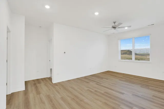 an empty room with wooden floor chandelier fan and windows