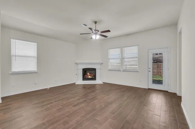an empty room with wooden floor a ceiling fan white walls and windows