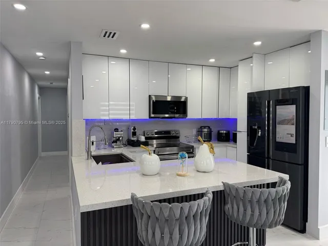 a kitchen with stainless steel appliances kitchen island granite countertop a refrigerator a stove a microwave oven a sink and a dining table with wooden floor