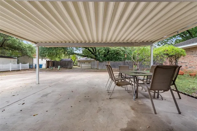 a view of a patio with table and chairs under an umbrella with a large tree