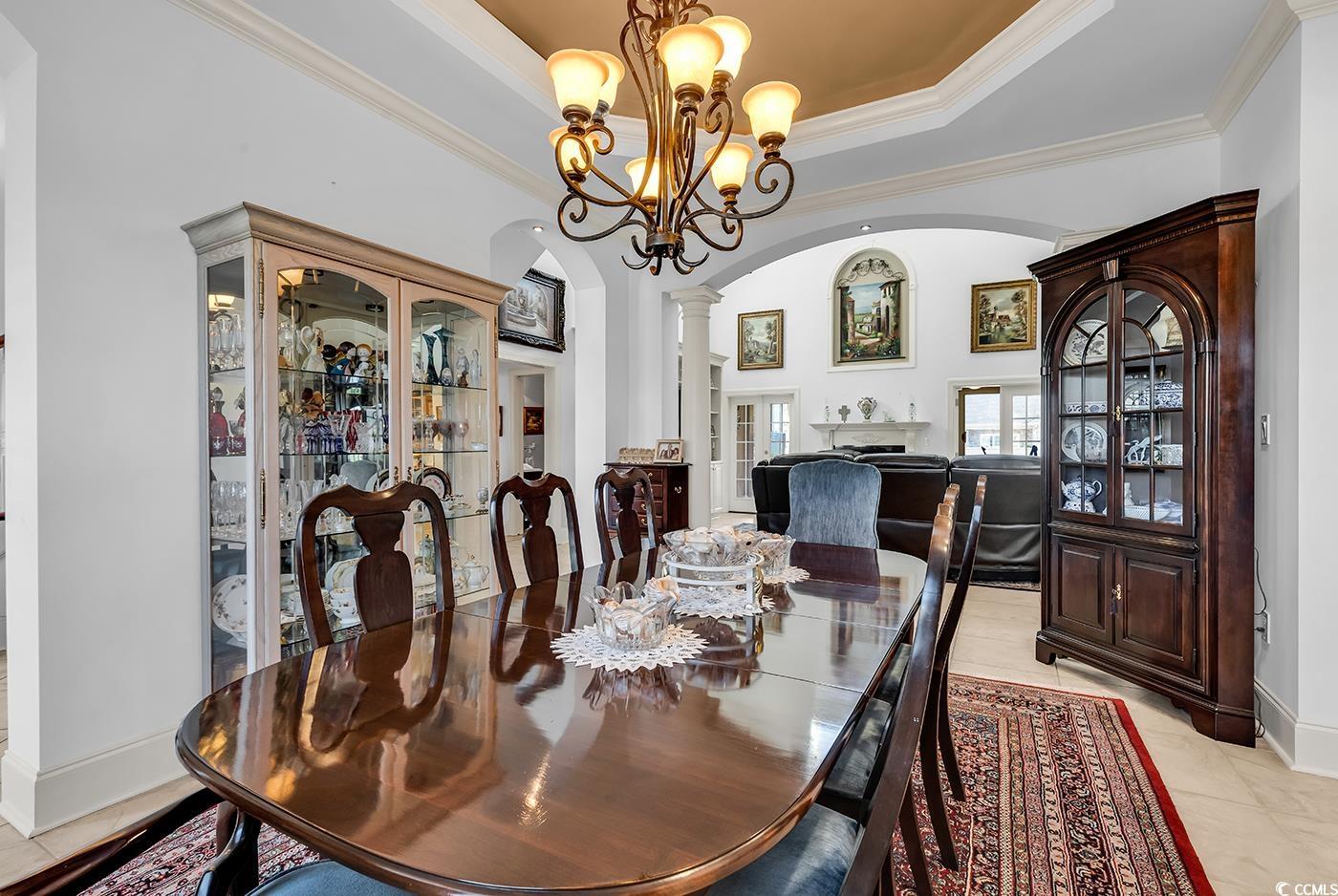 801 Bluffview Drive Myrtle Beach, SC 29579 - Photo 7 of 40 Dining area featuring arched walkways, a tray ceiling, decorative columns, crown molding, and light tile patterned floors