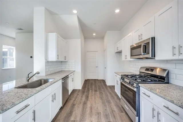 a kitchen with granite countertop stainless steel appliances a sink cabinets and wooden floor