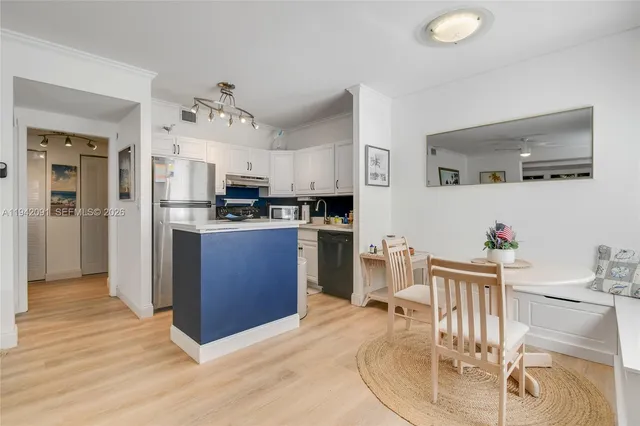 a kitchen with stainless steel appliances kitchen island granite countertop a refrigerator a stove top oven and a dining table with wooden floor