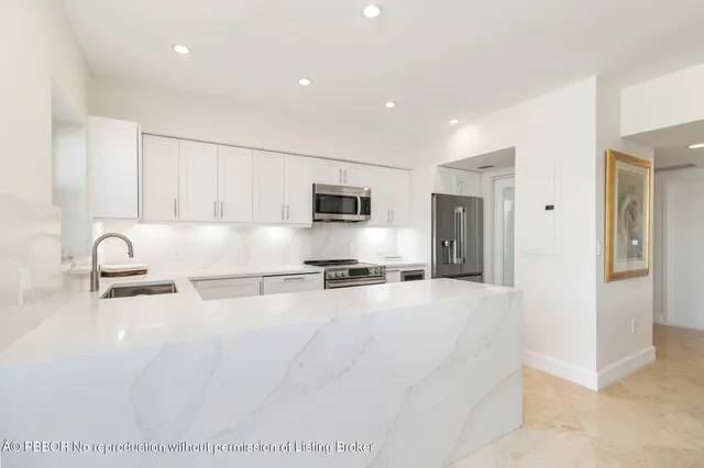 a large white kitchen with stainless steel appliances granite countertop a stove a sink a refrigerator and white cabinets with wooden floor