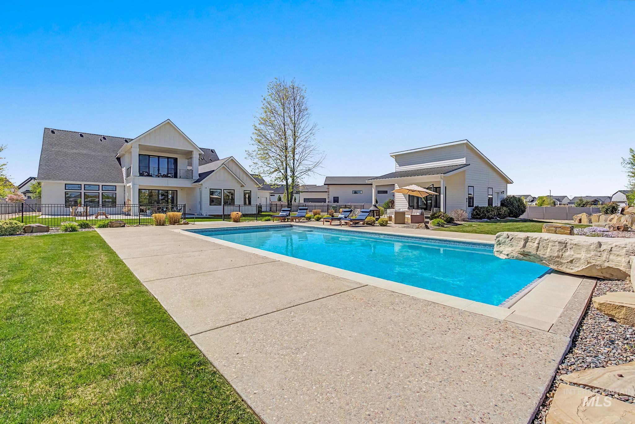 6521 South Pemberley Way Meridian, ID 83642 - Photo 1 of 42 Expansive backyard featuring a large in-ground swimming pool with concrete decking, a manicured lawn, and a modern white-sided residence with multiple large windows and a second-story balcony