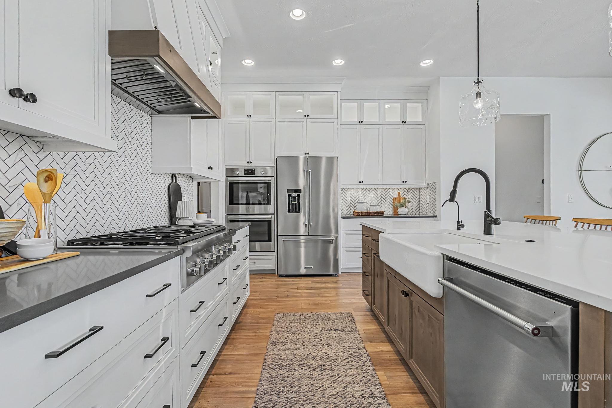 6521 South Pemberley Way Meridian, ID 83642 - Photo 17 of 42 Contemporary kitchen featuring white cabinetry, a large center island with a farmhouse sink, stainless steel appliances, and wood-finish flooring