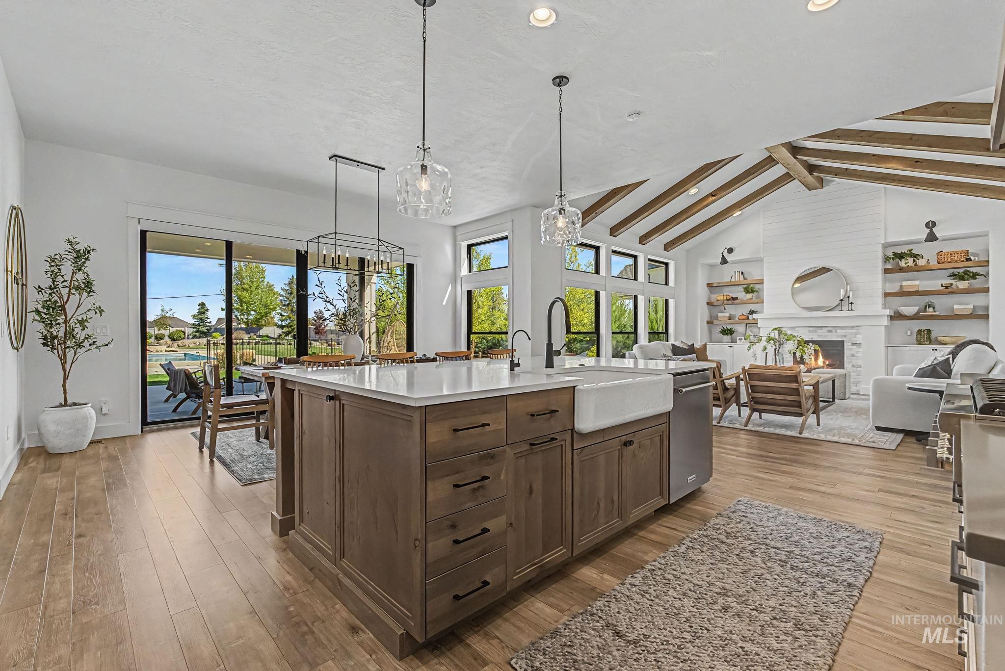 6521 South Pemberley Way Meridian, ID 83642 - Photo 18 of 42 Open-concept living space with wood-finish flooring, a kitchen island featuring a farmhouse sink and integrated dishwasher, and a living area with a vaulted ceiling and exposed beams