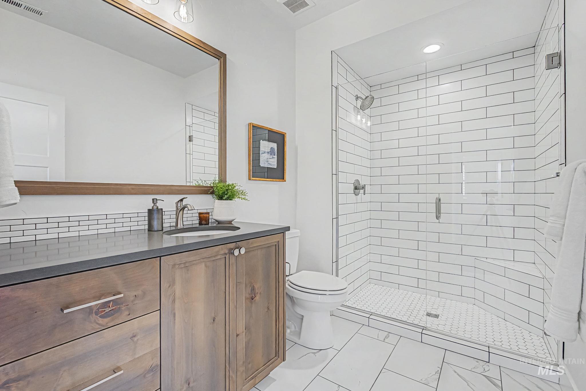 6521 South Pemberley Way Meridian, ID 83642 - Photo 28 of 42 Bathroom featuring a glass-enclosed shower with subway tile surround, a wood-finish vanity with a dark countertop, white subway tile backsplash, and a large framed mirror