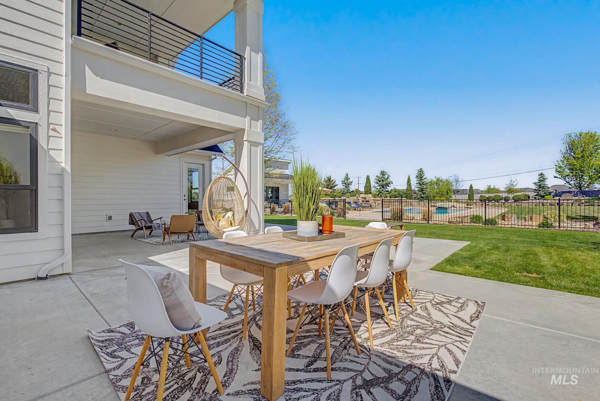 6521 South Pemberley Way Meridian, ID 83642 - Photo 31 of 42 Expansive concrete patio with a covered outdoor area, featuring a second-story balcony with black metal railings, a manicured lawn, and a black wrought-iron fence