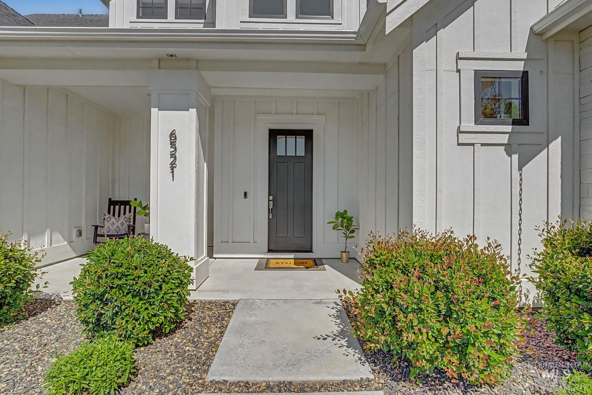 6521 South Pemberley Way Meridian, ID 83642 - Photo 4 of 42 Covered entryway featuring a dark-paneled door with upper glass inserts, vertical board and batten siding, dark-trimmed windows, and a concrete pathway flanked by mature shrubs