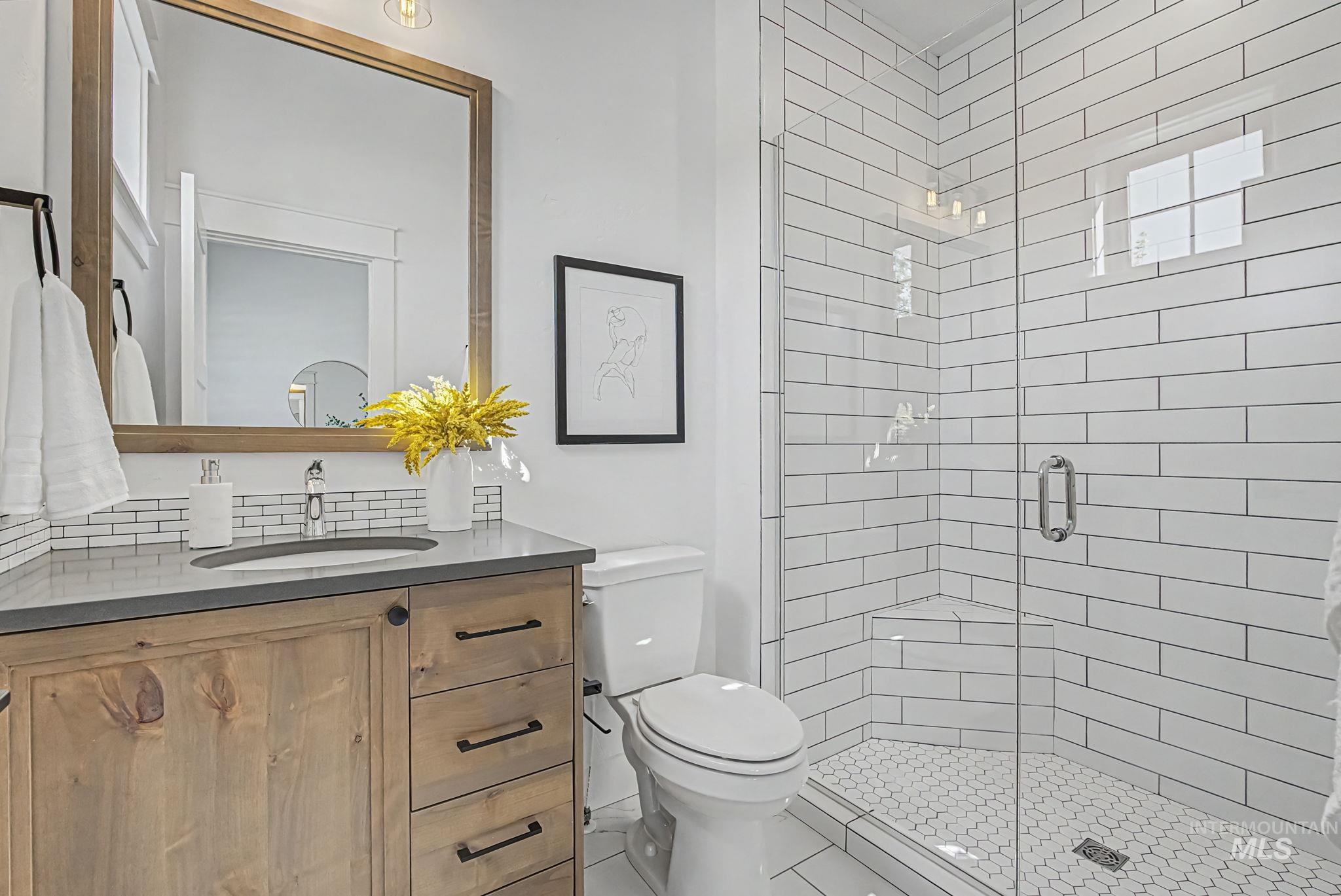 6521 South Pemberley Way Meridian, ID 83642 - Photo 9 of 42 Bathroom featuring a wood-finish vanity with a built-in sink, a framed mirror, and a walk-in shower with subway tile walls and a hexagonal tile floor