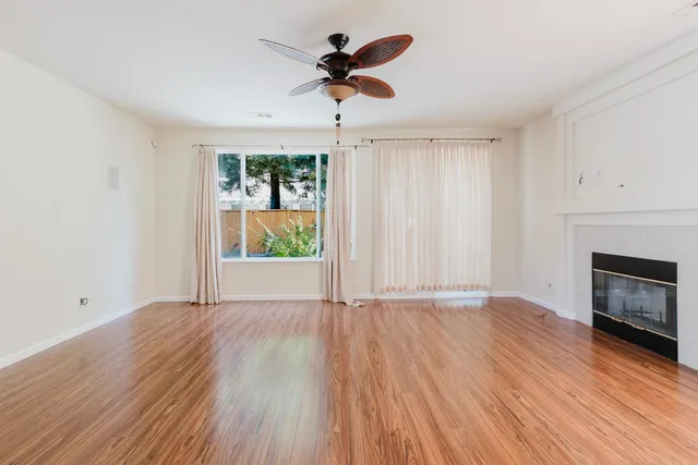 an empty room with wooden floor a ceiling fan and windows