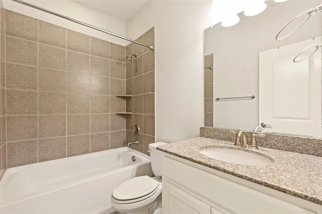 a bathroom with a granite countertop bathtub shower sink vanity mirror and toilet
