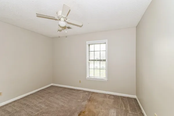 an empty room with chandelier fan and windows