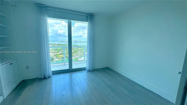 a view of an empty room with a window and wooden floor