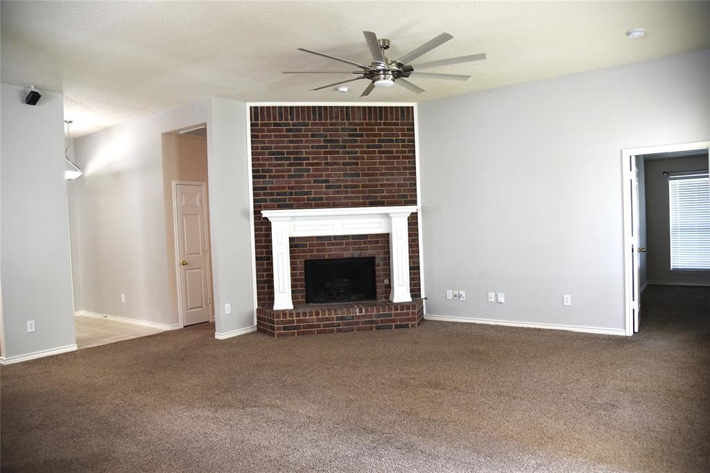 1526 Pebblestone Court Allen, TX 75002 - Photo 10 of 28 Spacious room featuring a brick fireplace with a white mantel, ceiling fan with brushed nickel accents, neutral carpet flooring, and light gray wall paint