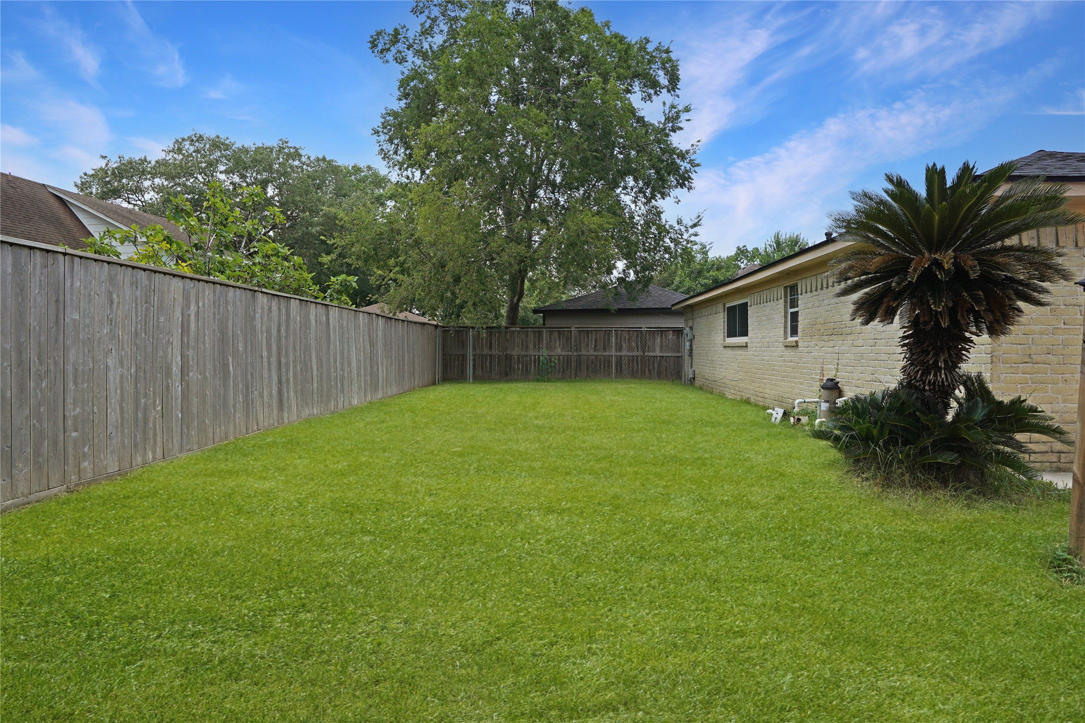 17119 Mellow Ridge Drive Spring, TX 77379 - Photo 30 of 32 Spacious backyard with a well-maintained lawn, bordered by a wooden fence. Features a mature tree and a small garden area next to the house, providing privacy and greenery.