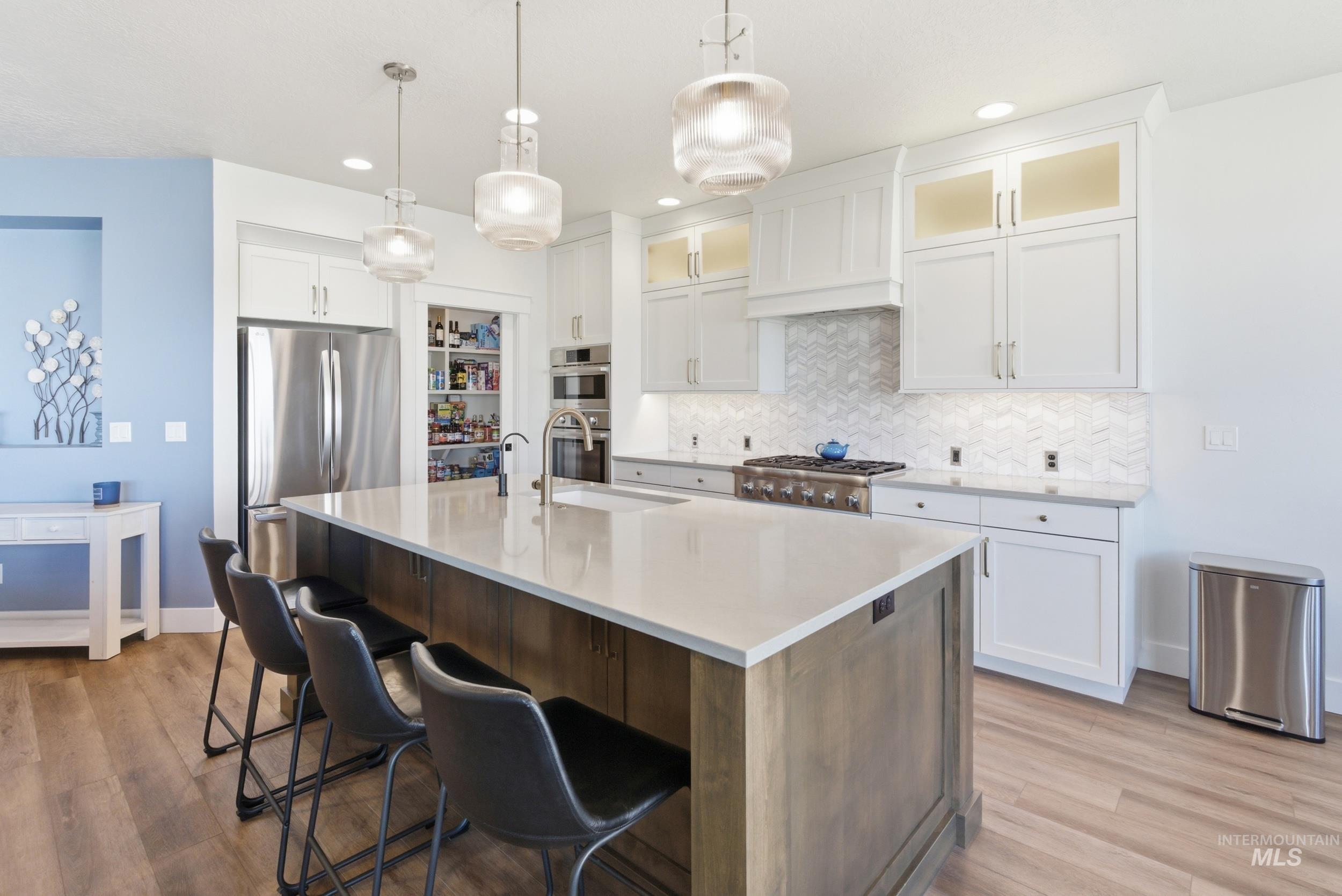 6347 South Utmost Lane Meridian, ID 83642 - Photo 2 of 37 Gourmet kitchen featuring a large central island with seating, stainless steel appliances, a five-burner gas range, white shaker cabinetry, and a herringbone tile backsplash