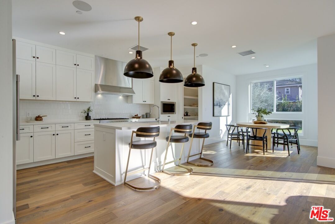 10810 Valley Spring Lane Studio City, CA 91602 - Photo 4 of 36 a kitchen with stainless steel appliances kitchen island wooden floors and white cabinets